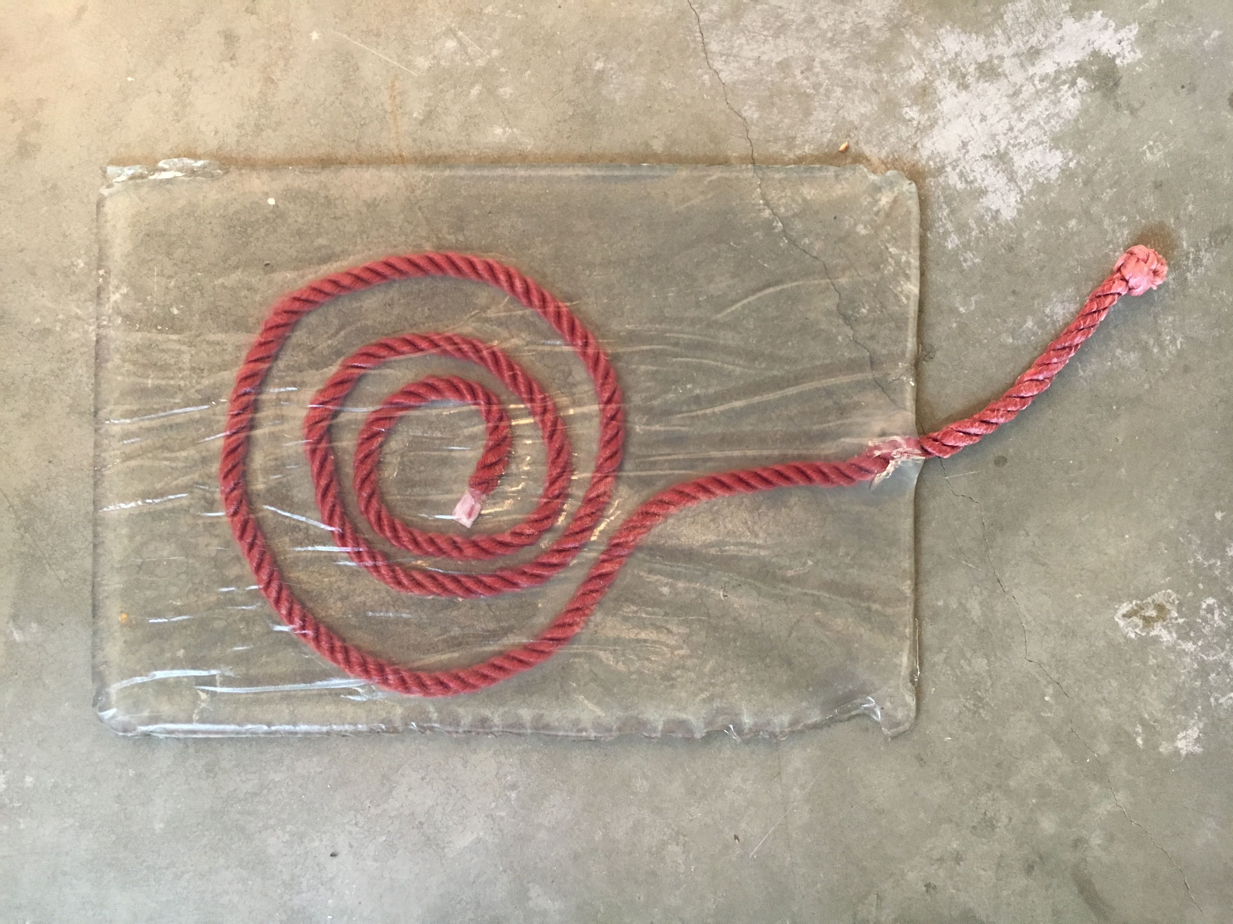from about, a gelatin rectangle with suspended pink coiled rope within,
                    on concrete